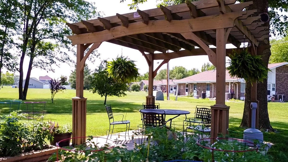 A wooden pergola providing shade over an outdoor seating area in a garden setting.