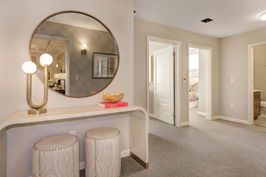 A modern hallway featuring a round mirror, console table, and stools with elegant decor.