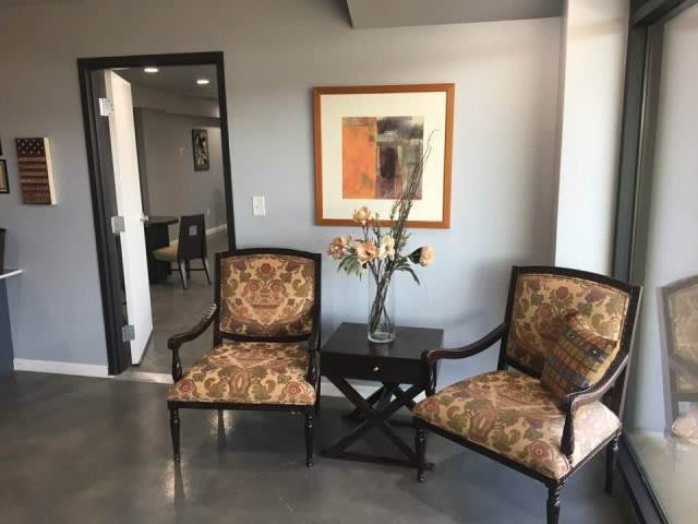 A cozy waiting area with two upholstered chairs and a side table, adorned with a vase of flowers and framed artwork on the wall.