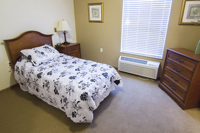 A cozy bedroom with a single bed, a nightstand with a lamp, and a window with blinds.