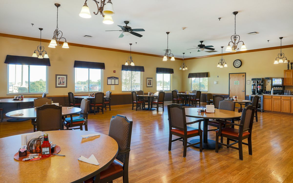 A spacious dining area with multiple tables and chairs, ceiling fans, and warm lighting.