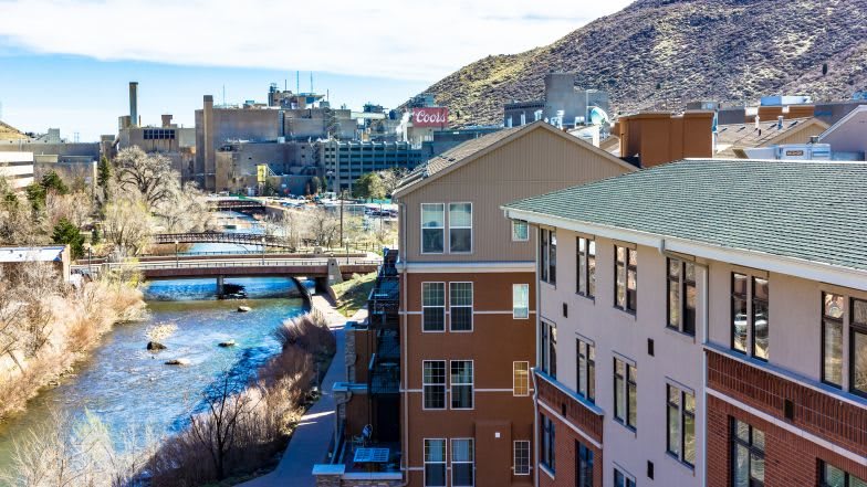 A scenic view of urban buildings along a river, with a bridge and mountains in the background.