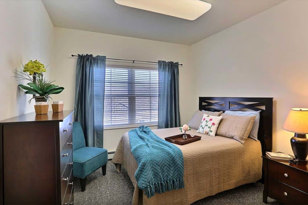 A cozy bedroom with a neatly made bed, teal accents, and natural light streaming through the window.