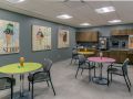 A colorful breakroom with tables, chairs, and artwork on the walls.
