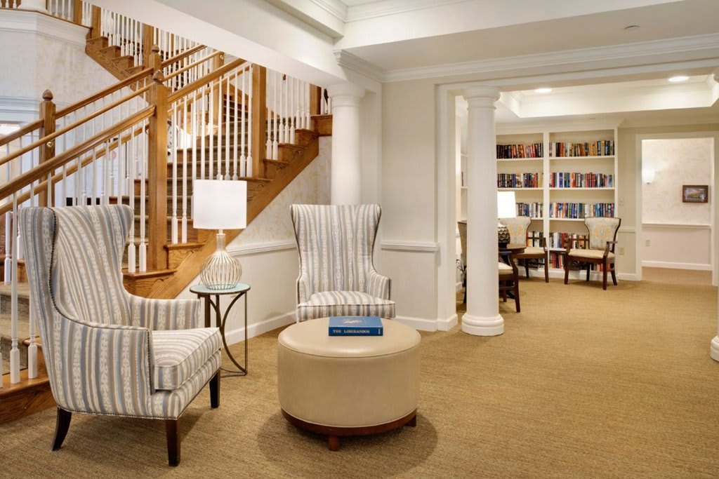 A cozy living room with armchairs and a staircase leading to the upper floor, featuring bookshelves and ambient lighting.