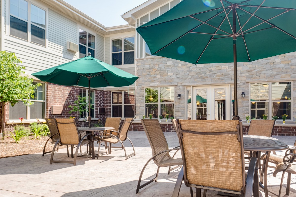 An outdoor patio area with tables, chairs, and green umbrellas in front of a building.