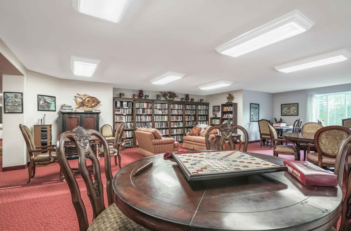 A cozy library room featuring bookshelves, comfortable seating, and a central table.