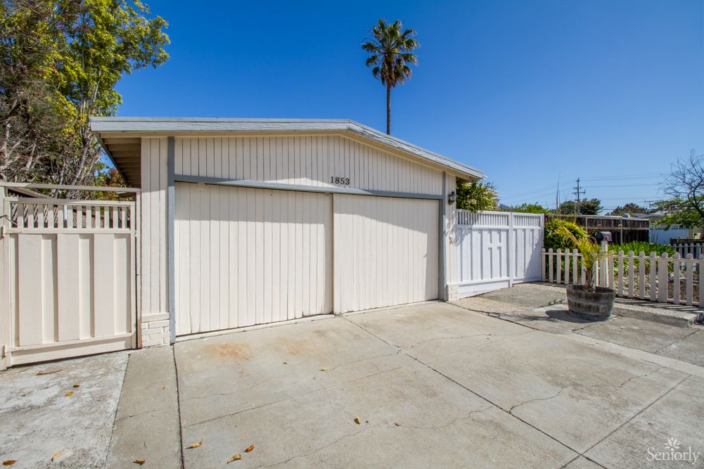 A residential garage with a driveway under a clear blue sky and a palm tree in the background.