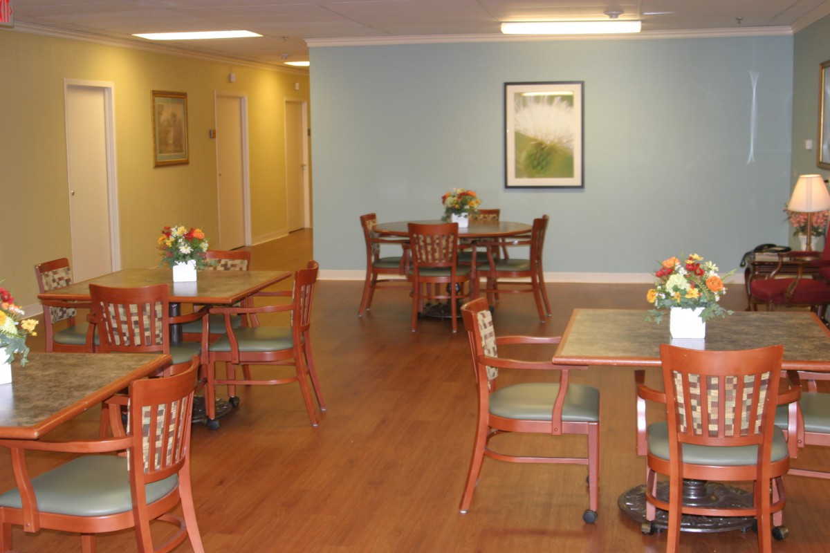 A cozy dining room with wooden tables and chairs, decorated with flowers and artwork on the walls.