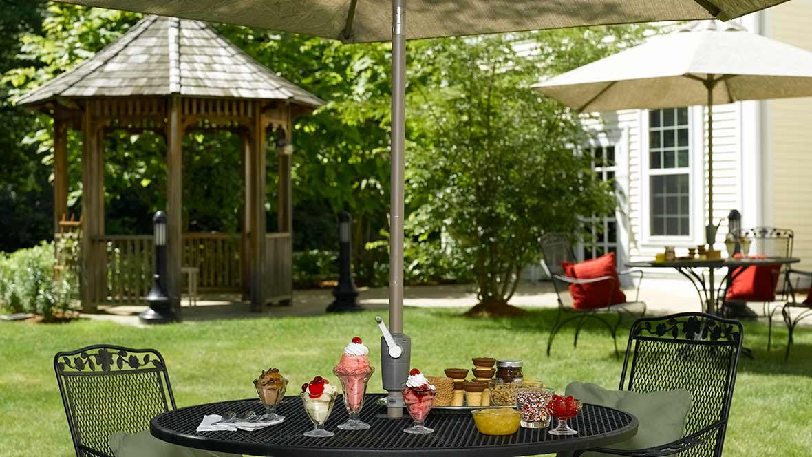 A garden patio scene with a table under an umbrella, displaying various desserts and snacks.