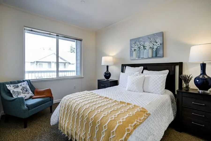 A cozy bedroom with a neatly made bed, a lamp on the bedside table, and artwork above the headboard.