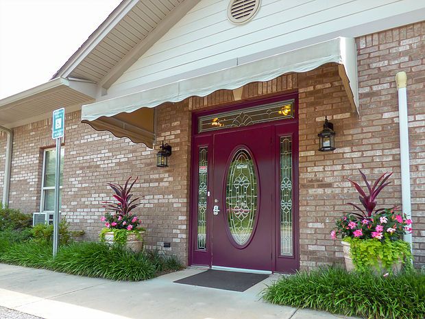 A front entrance with a maroon door, brick facade, and decorative plants.