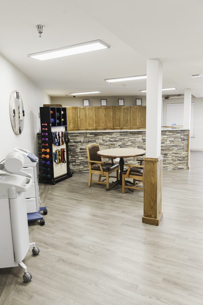 A modern basement kitchenette featuring a stone accent wall, wooden cabinets, a round table with chairs, and a wine rack.
