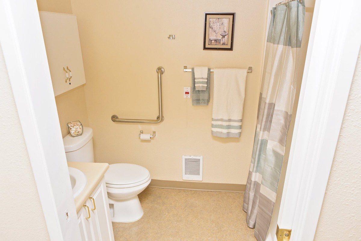 A bathroom featuring a toilet, sink, and shower with a curtain, along with towels and wall art.