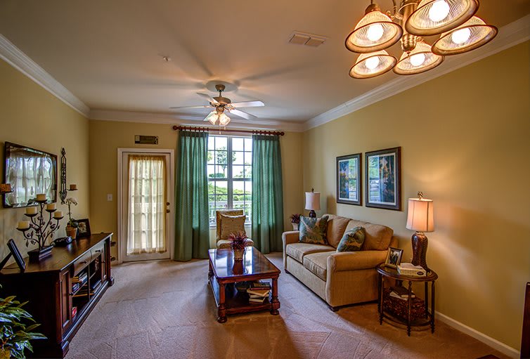 A cozy living room with a sofa and coffee table, featuring green curtains and warm lighting.