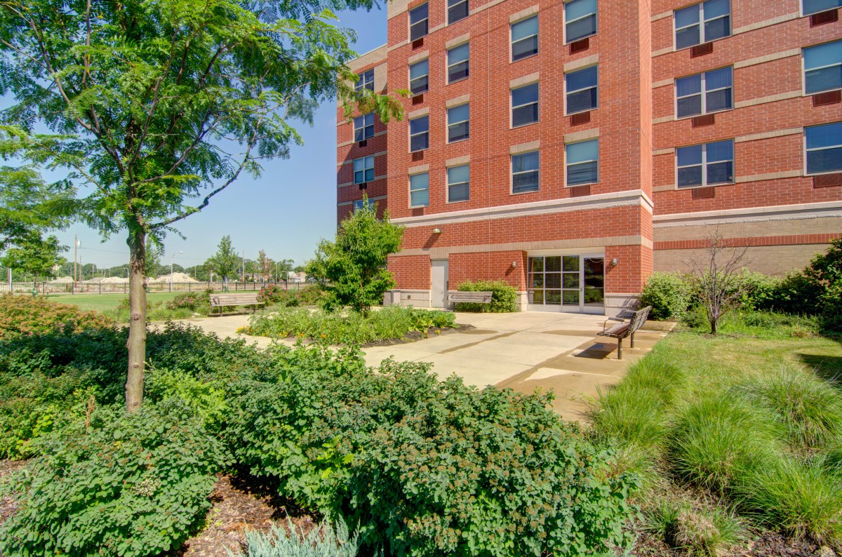 A sunny day view of a brick building with lush landscaping and a pathway.