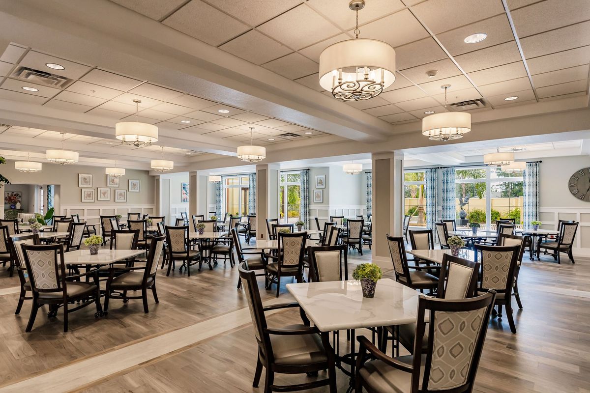 An elegant dining area with neatly arranged tables and chairs, illuminated by chandeliers.