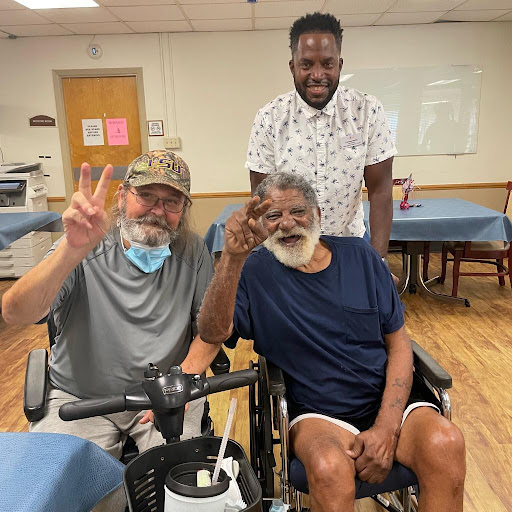 Three friends enjoying a moment together in a care facility, sharing smiles and peace signs.
