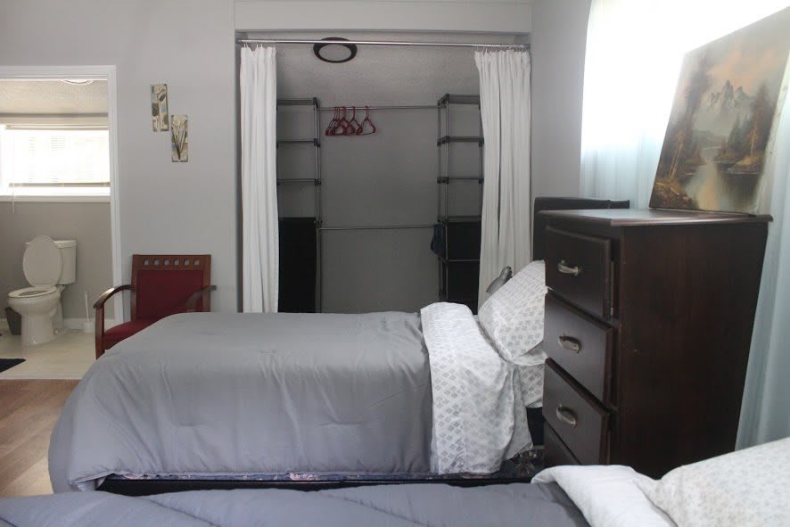 A bedroom with two neatly made beds, a dresser, and an open closet.