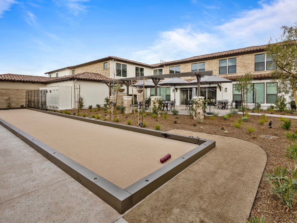 A residential backyard featuring a bocce court and a modern house.