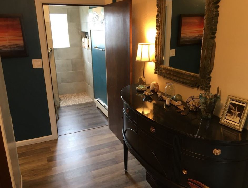 A cozy hallway with wood flooring, featuring a stylish dresser and mirror, leading to a bathroom.