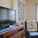 A cozy living room featuring a TV, wooden cabinet, and an armchair with a colorful quilt.