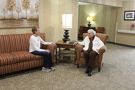 A caregiver and an elderly woman engaged in conversation in a cozy indoor setting.
