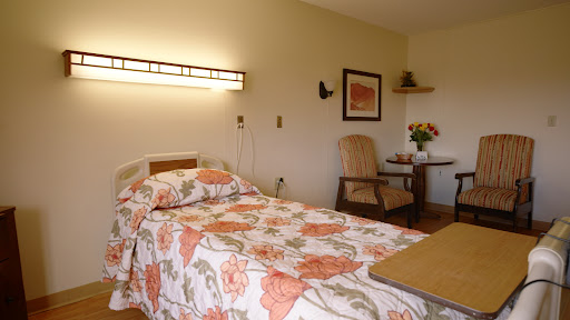 A cozy hospital room featuring floral bedding, a comfortable chair, and soft lighting.