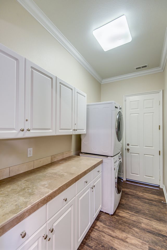 A compact laundry room with stacked washer and dryer, surrounded by white cabinets for storage.