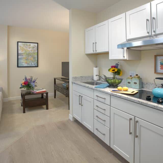 A modern kitchen with white cabinetry and a cozy dining area in an apartment setting.