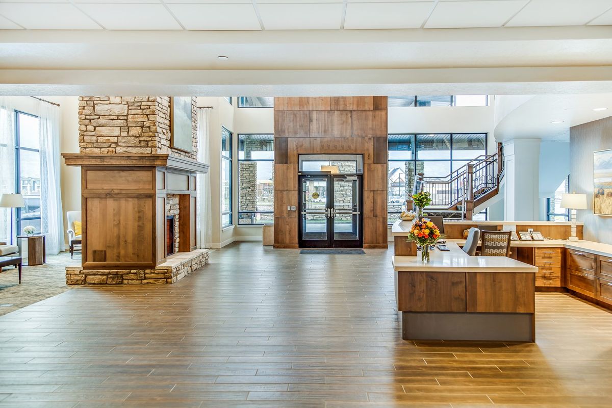 A spacious and modern lobby featuring a fireplace, wood paneling, and a reception desk with large windows providing ample natural light.