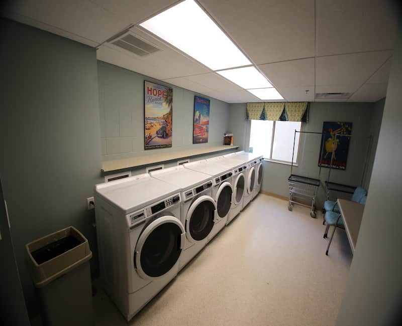 A clean, well-lit laundry room featuring several washing machines along the wall.