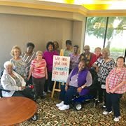 A group of seniors gathered indoors, with a sign in the center.