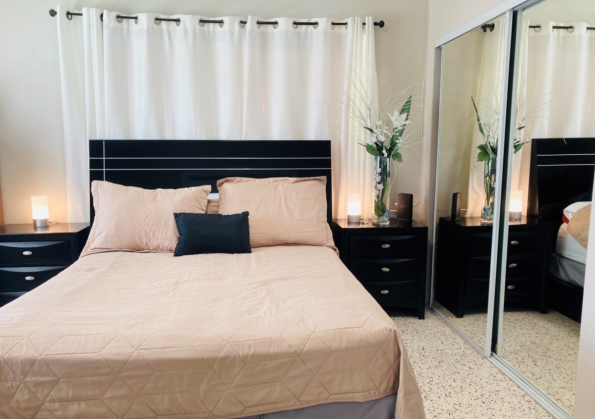 A cozy bedroom with modern and minimalist decor, featuring a neatly made bed, mirrored closet doors, and stylish nightstands.