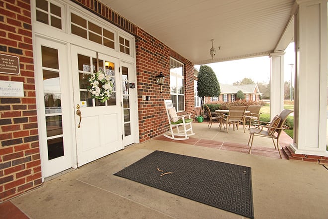A welcoming porch with a rocking chair, patio furniture, and a wreath on the door.