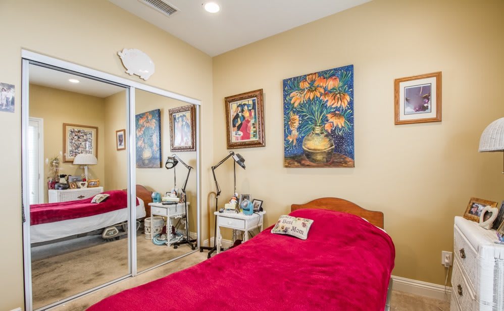 A cozy bedroom with a single bed featuring red bedding, adorned with vibrant paintings and reflective mirror closet doors.
