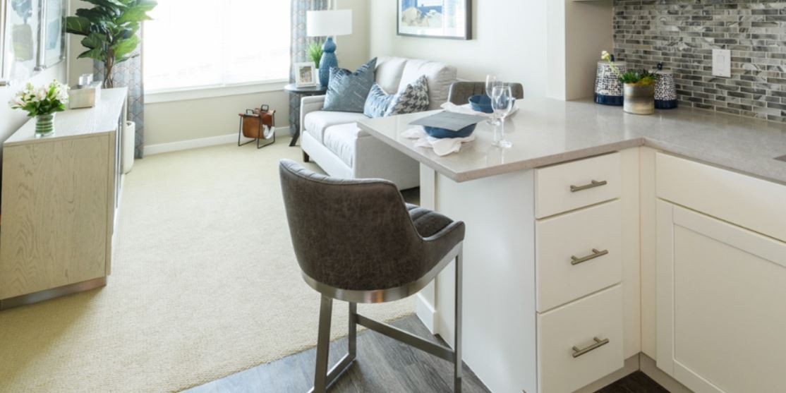 A modern living room with a sofa, decorative cushions, and a high chair next to a countertop.