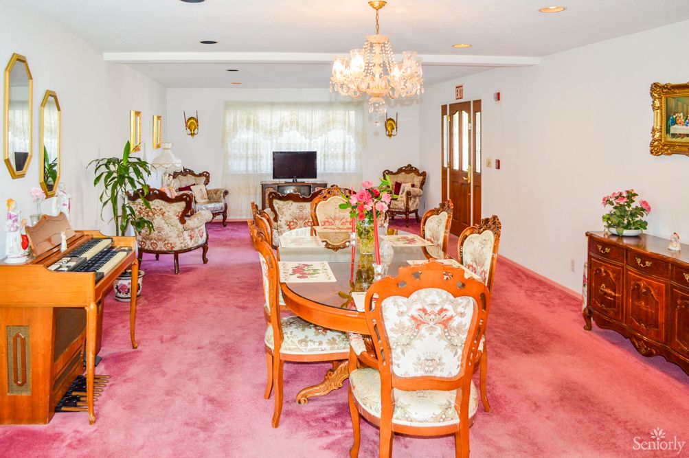 A vintage-style dining room with a pink carpet, elegant chandelier, and floral upholstered furniture.