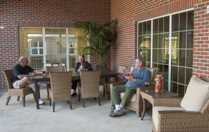 A group of people relaxing on a patio with wicker furniture and a brick wall backdrop.