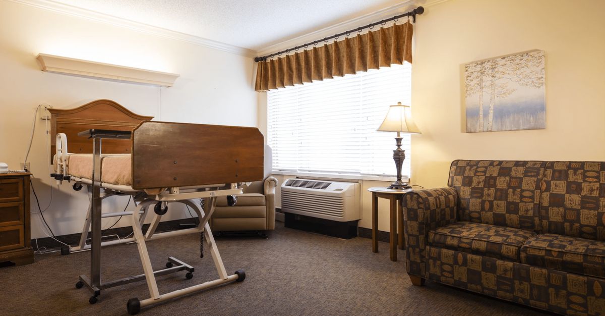 A hospital room with a medical bed, armchair, and lamp by the window.