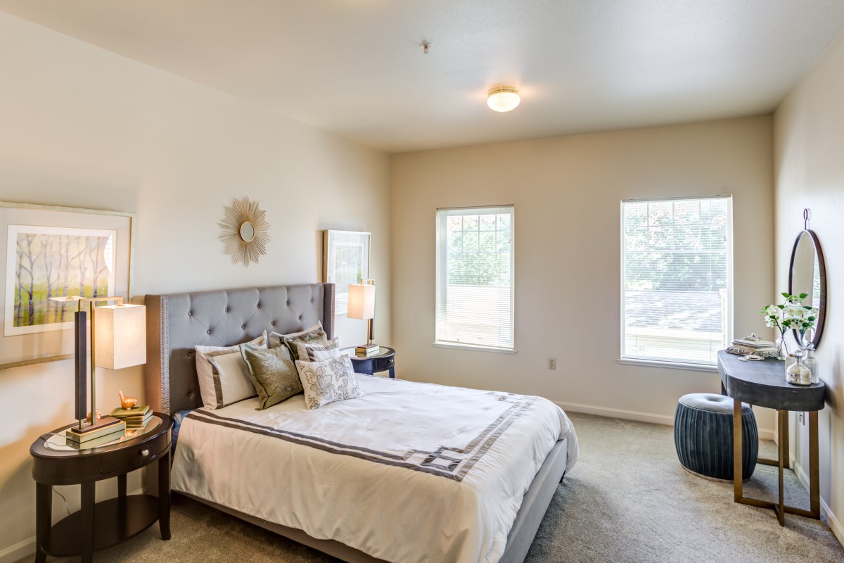 A modern bedroom with a neatly made bed, stylish decor, and ample natural light from two windows.