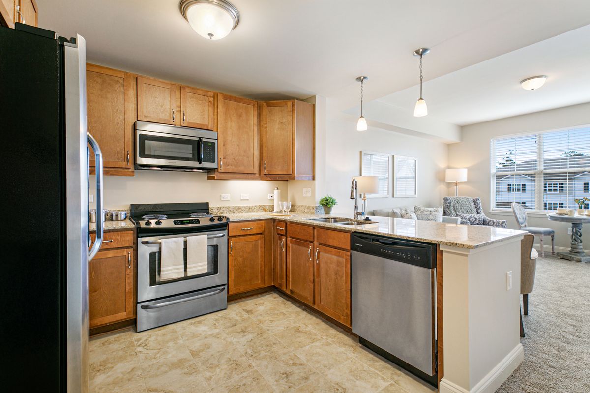 A modern kitchen with stainless steel appliances and wooden cabinets, featuring an open floor plan with ample lighting.