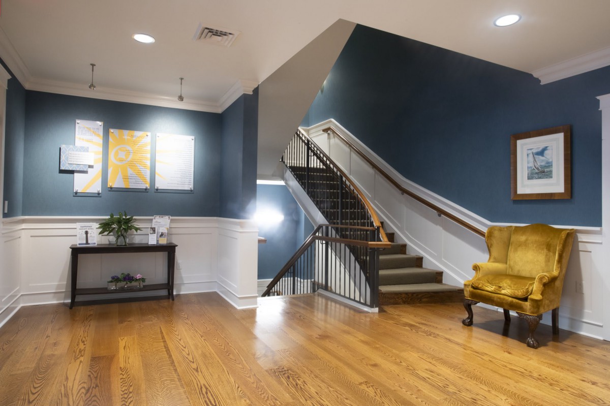 A modern interior featuring a staircase with wooden steps, navy blue walls, and artwork. The room is well-lit with stylish decor and seating.