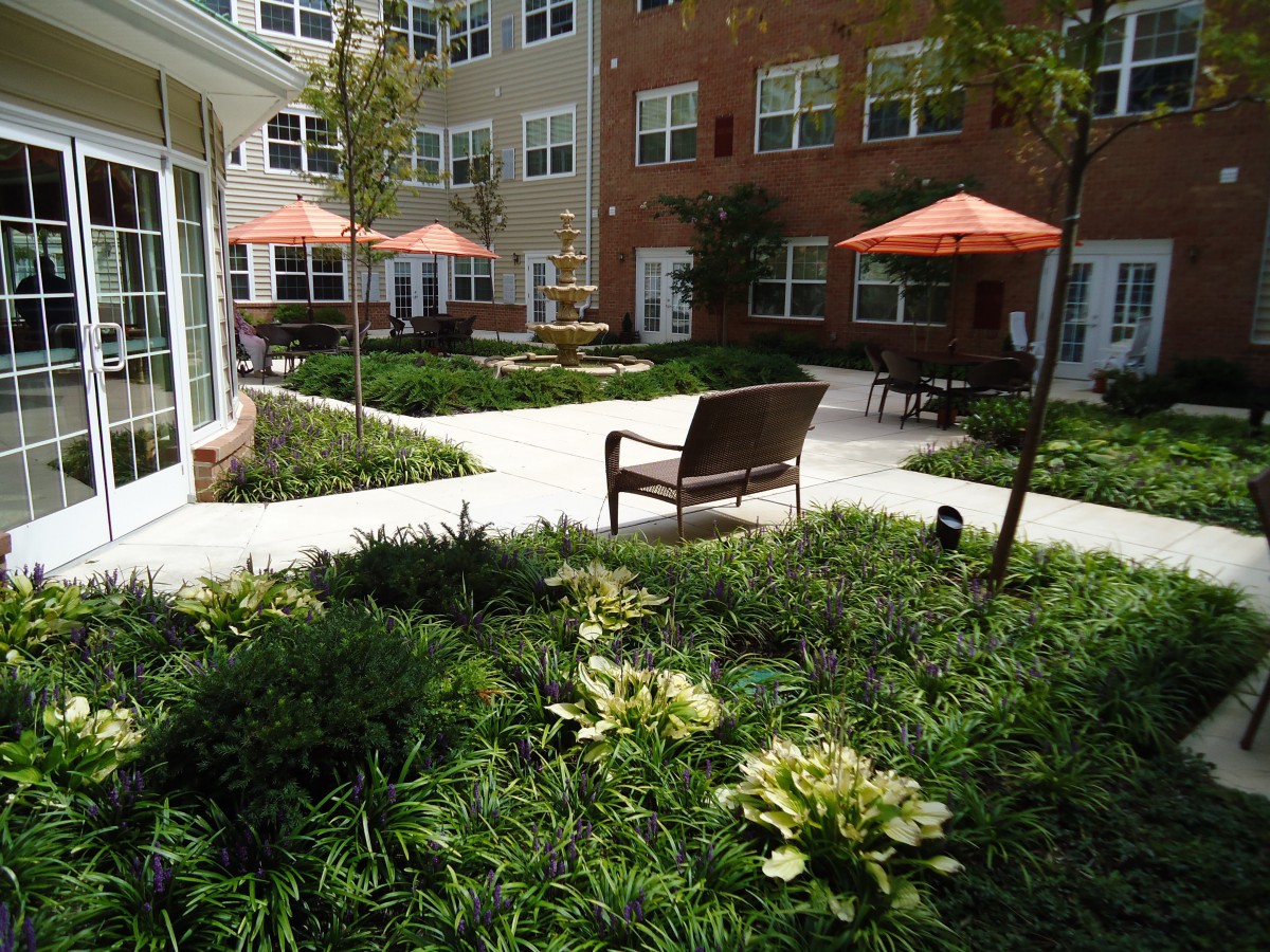 A peaceful courtyard in an apartment complex featuring benches, greenery, and orange umbrellas.