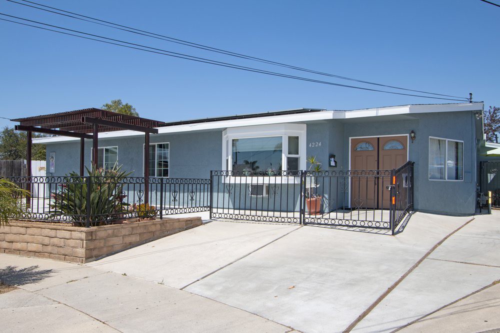 A single-story residential house with a driveway and fenced front yard.