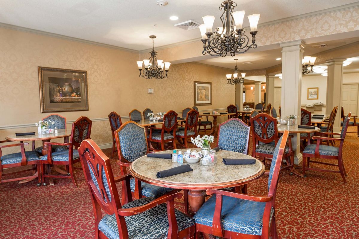 An elegant dining room with upholstered chairs and chandeliers.