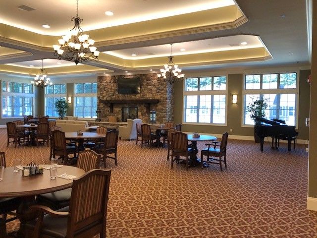 A spacious dining room with wooden furniture, chandeliers, a grand piano, and a cozy fireplace.