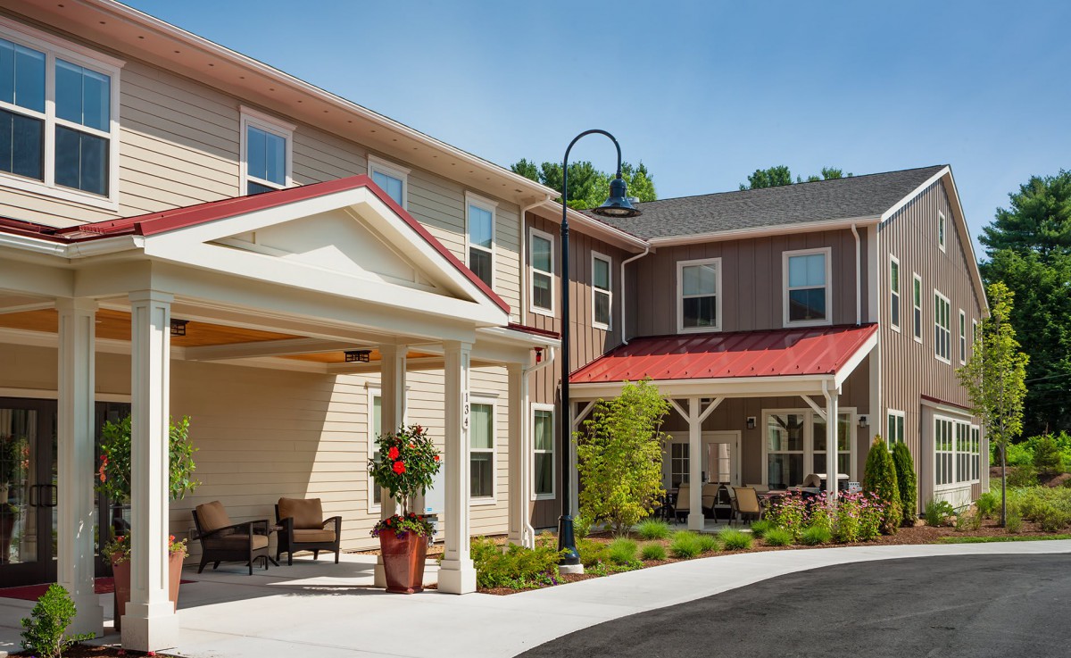 A modern residential building with a covered porch and well-maintained landscaping, photographed on a clear day.