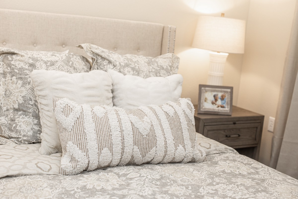 A cozy bedroom setup featuring decorative pillows, elegant bedding, and a lit lamp on the bedside table.