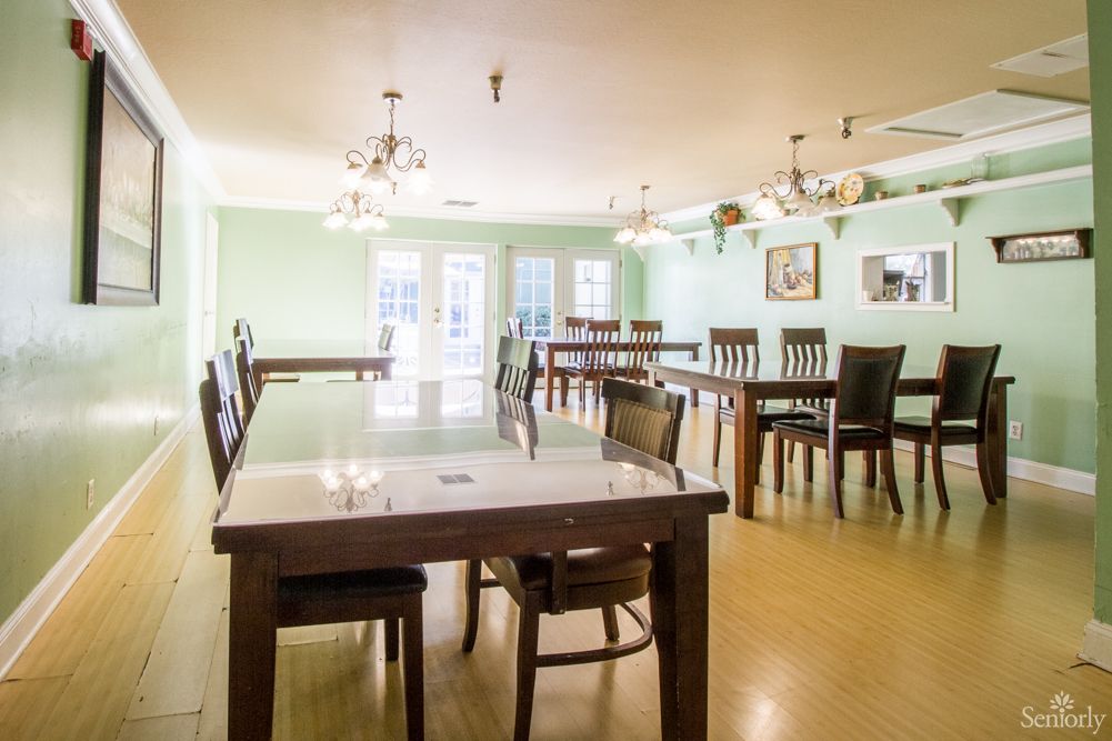 A spacious dining room with multiple tables and chairs, featuring elegant chandeliers and a wooden floor.